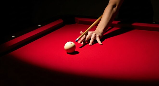 Hand aiming billiard ball on red pool table with cue stick in dark room; professional precision shot in a billiards game