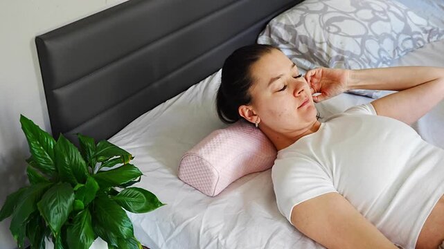 Woman lying on ergonomic orthopedic pillow on bed. Demonstrating cervical spine support, proper neck alignment and comfortable sleep for posture correction and pain relief at home.