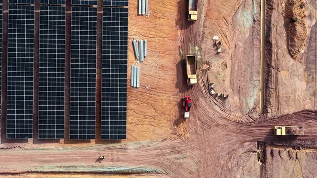 Aerial drone view of solar farm construction with panels, trucks and earthworks in desert landscape.