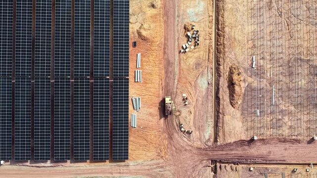 Aerial drone shot of solar farm construction site showing panel arrays and earthmoving activity.