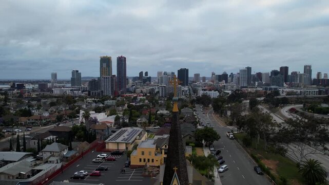 Cinematic drone pullback above a church with the San Diego skyline in the background at 7PM during sunset. Warm evening light highlights architectural details and the city beyond.