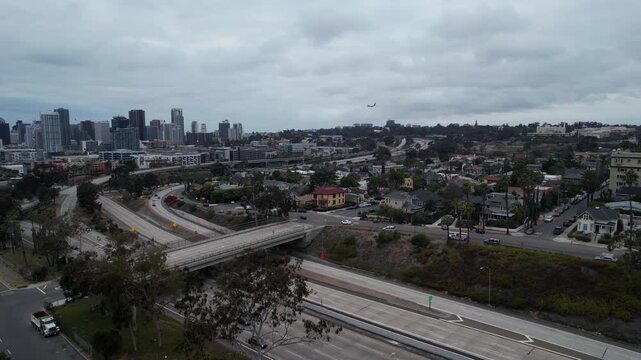 Aerial drone flying toward Interstate 94 in San Diego at 7PM during sunset as an airplane descends for landing in the background. Traffic flows along the freeway under warm evening light.