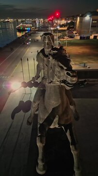 Vertical aerial night view circling the famous illuminated equestrian statue of Alexander the Great on the waterfront of Thessaloniki, Greece.