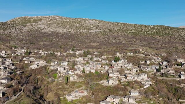 Slow panning drone shot of Kalarrytes mountain village in Epirus, Greece, surrounded by rugged peaks and greenery