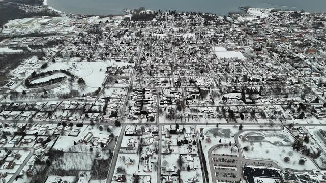 Aerial drone view flying forward over a plattsburgh, new york covered in a fresh layer of white snow during a cloudy winter day, showing residential houses, streets, parks, and the waterfront