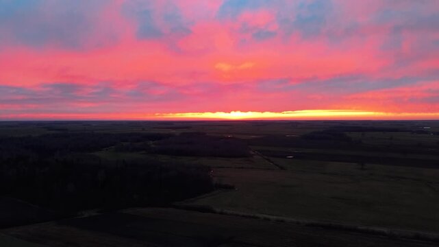 Drone video capturing a breathtaking sunset over lush green fields, with vivid pinks and oranges coloring the sky. The landscape stretches toward the horizon, showcasing serene beauty.