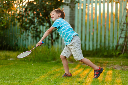 A young boy engaged in active badminton play outdoors on a sunny summer day. Dynamic movement, coordination, and fun leisure time during holidays in a green park.