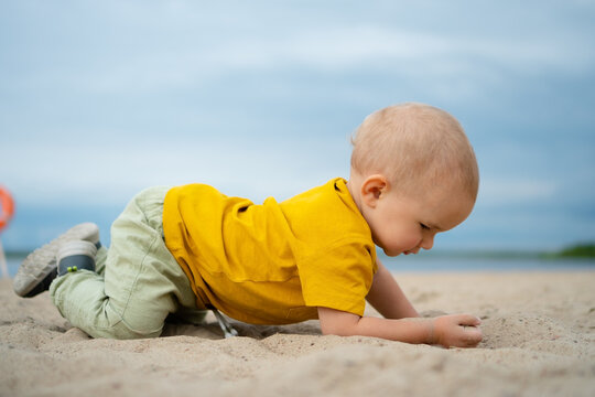 A happy toddler in a yellow shirt discovers the texture of sand on a bright beach day, embodying the wonder and excitement of exploring nature playground.