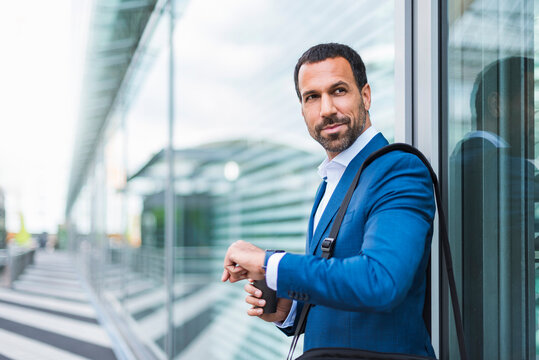 Businessman in blue suit checking time outside modern office