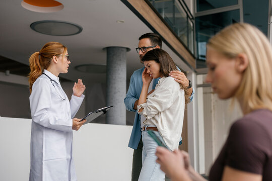 Doctor consulting patient and partner in clinic hallway