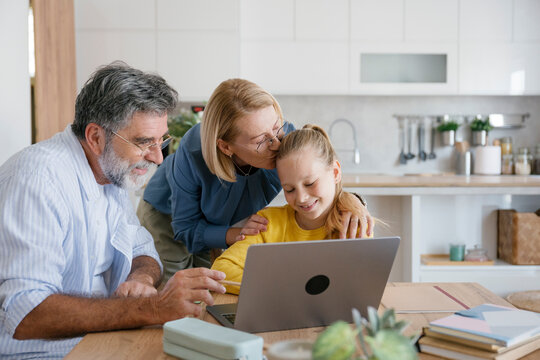 Grandparents helping girl with homework on laptop at home