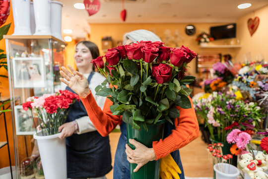 Florist holding red rose bouquet in flower shop with smiling assistant