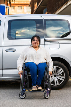 Portrait of woman in wheelchair outdoors by vehicle promoting mobility