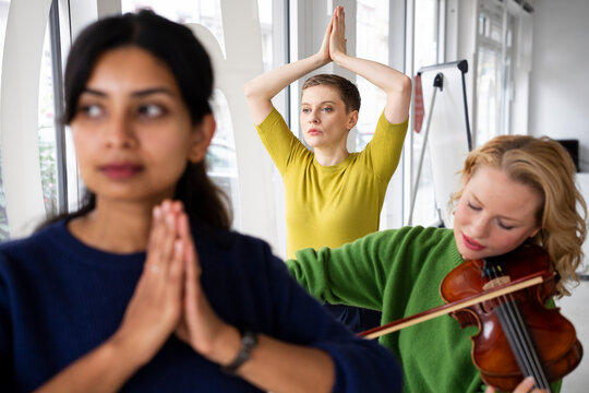 Women practicing yoga and playing violin in an office setting