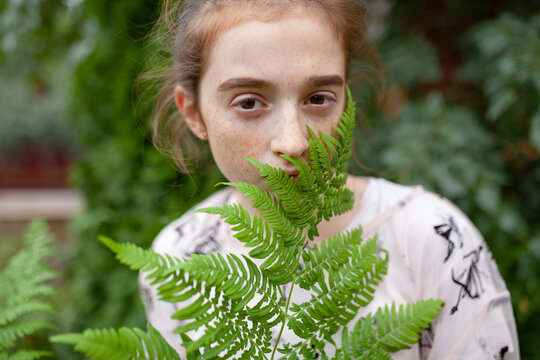 Freckled teenager looking at camera behind fern outdoors in summer