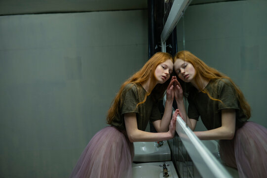 Red haired woman in vintage bathroom leaning on mirror with reflection