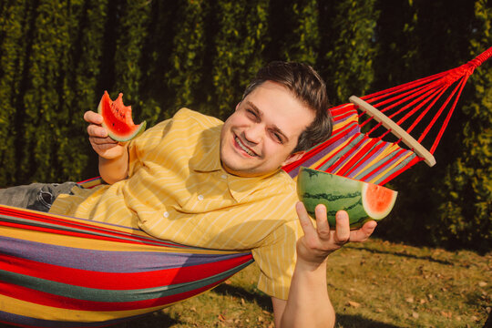 Smilingman relaxing in hammock eating watermelon outdoors