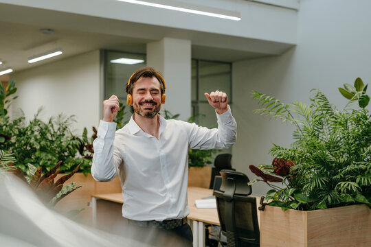 Businessman enjoying music and dancing in a modern office with plants
