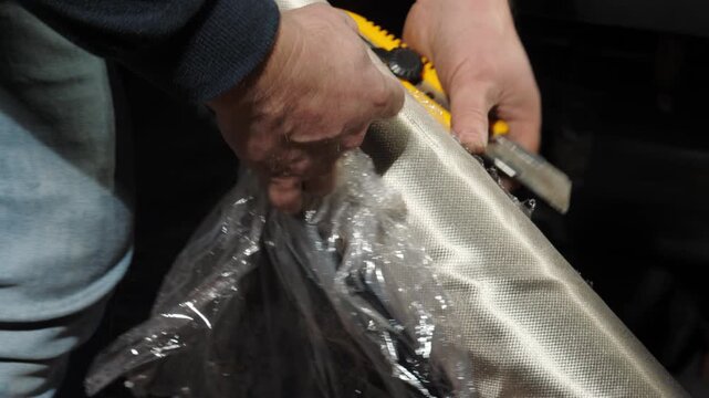 Man takes plastic foil out of electromagnetic field shielding fabrics roll in storage closeup. Employee unpacks EMF radiation reducing textile