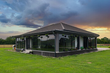 Obraz premium Modern glass house with enclosed veranda on a green lawn at sunset in the countryside