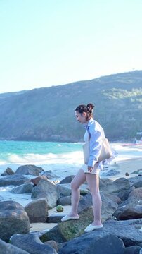 Asian woman enjoying summer vacation at the beach, wearing sun hat and sunglasses, smiling with blue ocean background