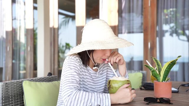 Asian woman enjoying fresh coconut drink at tropical resort, relaxing during summer vacation travel lifestyle