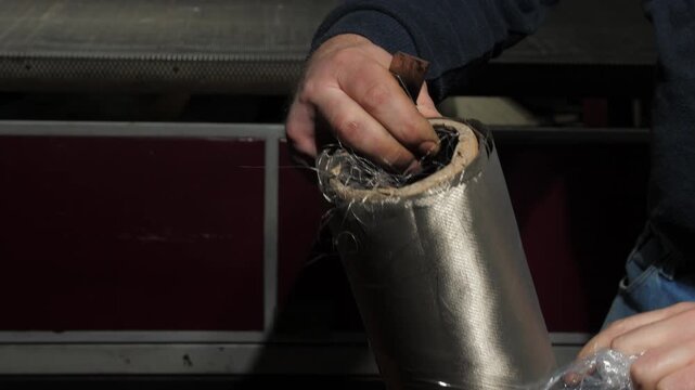 Employee unpacks roll of EMF radiation shielding fabric. Man removes protective plastic foil to reveal textile to block harmful electromagnetic fields