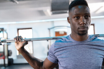 Adult male holding loaded barbell across upper back at gym wearing heather-blue shirt, copy space © wavebreak3