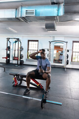 African American man wearing sportswear sitting on red bench in gym holding shaker near loaded bar © wavebreak3