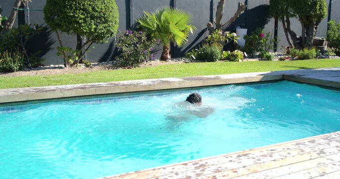 African American adult male running and jumping from wooden deck into backyard pool making splash