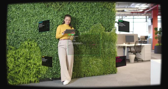 Leaning woman tapping tablet in office near green wall, in mustard top, engaging EXEC DASH panels