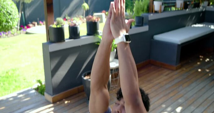 African American man in gray tee adjusting on deck mat, raising hands into prayer, meditating