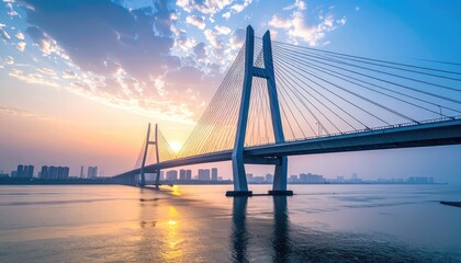 Obraz premium A stunning panoramic view captures a modern suspension bridge gracefully spanning a wide river at sunrise, with a cityscape visible in the distance under a vibrant sky.