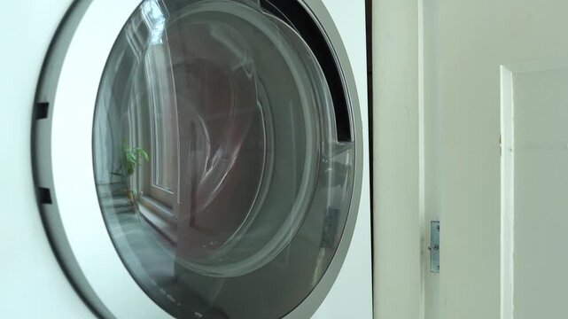 Colored laundry spins inside a washing machine drum, with color catcher sheets visible among the clothes to prevent dye transfer. Household appliance advertising, laundry detergent marketing