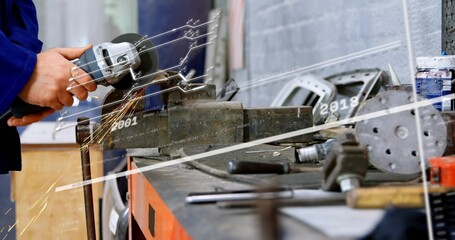 Fototapeta premium Grinding worker's hands in blue jacket using angle grinder on metal in workshop vise, sparks flying