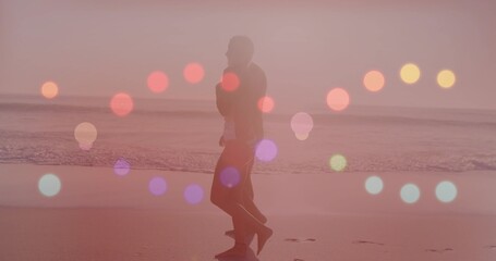 Fototapeta premium Walking couple wearing casual clothes strolling along wet shoreline at sunset, bokeh orbs