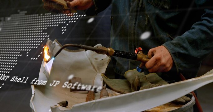 Operating handheld torch, technician in dark jacket heating curved white panel on drum with gloves