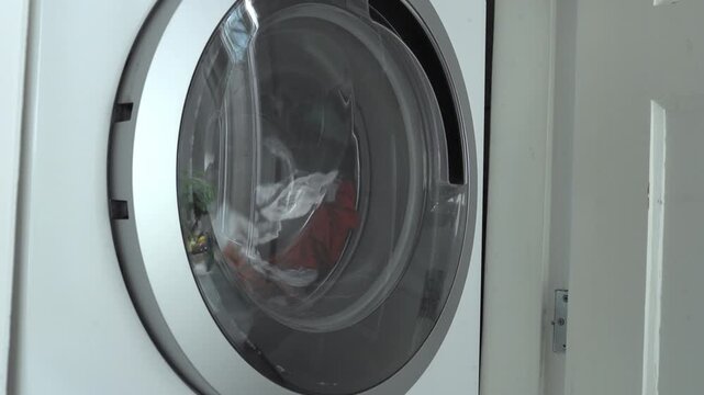 Colored laundry spins inside a washing machine drum, with color catcher sheets visible among the clothes to prevent dye transfer. Household appliance advertising, laundry detergent marketing