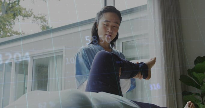 Holding Korean therapist in blue tunic helping bent leg on treatment table near sliding doors, grid