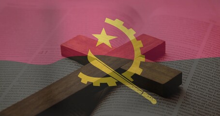 Obraz premium Lying wooden Christian cross casting soft shadow across open book on tabletop, Angola flag overlay