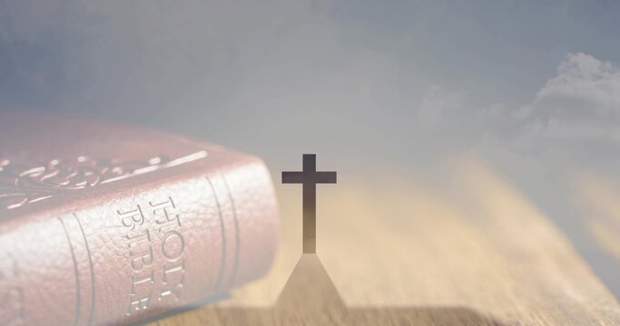 Casting simple cross silhouette creating long shadow on wooden tabletop, with leather Holy Bible