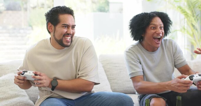 Diverse friends playing game on couch, reacting after game event, cheering with white controllers