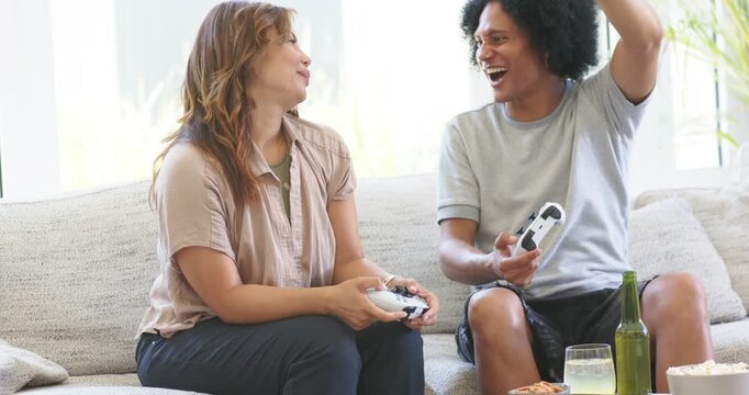 African American couple celebrating after scoring while holding white controllers on sofa at home