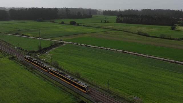 Aerial view of a vibrant yellow and black subway cutting through lush green fields, creating a striking contrast of color and form, Vila do Conde, Portugal.