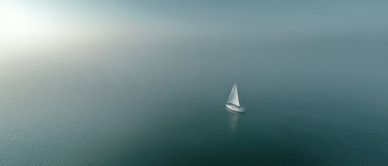 Fototapeta premium Aerial drone view of tiny white sailboat on glassy calm ocean with soft pastel mist and pale horizon