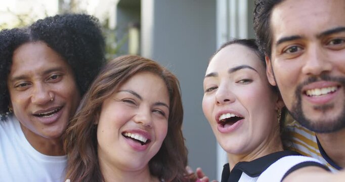 Diverse friends holding smartphone at arm's length, gathering tightly and singing for porch selfie