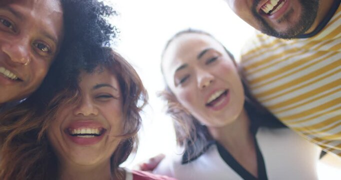 Diverse friends drawing to low camera linking arms, laughing and singing outdoors under bright sky