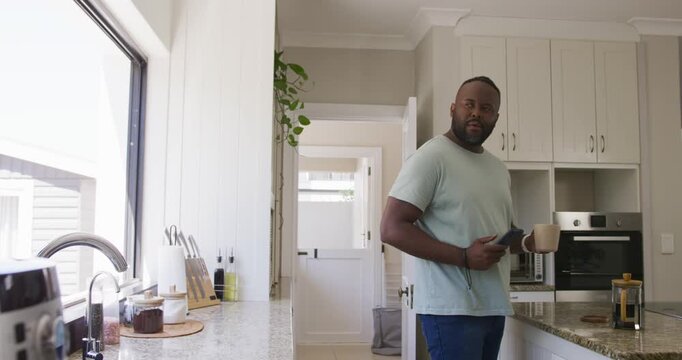Vertical video: Reaching man in green T making brew in kitchen holding mug phone and gazing window