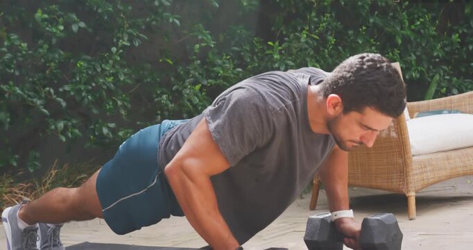 Man starting high plank in sportswear, doing push-ups on hex dumbbells for strength on patio mat