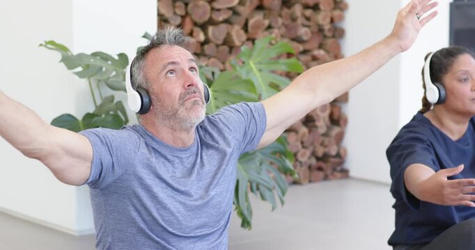Diverse partners following audio in white headphones on mats man lifting arms overhead into prayer